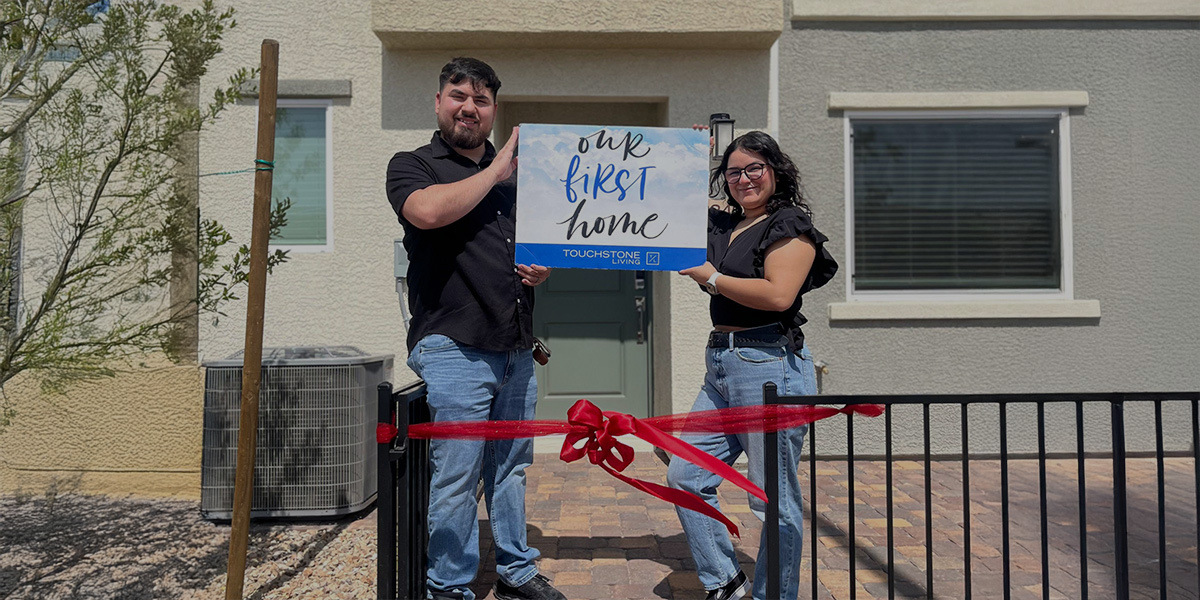 A man and woman in their 20s proudly holding a sign that says our first home