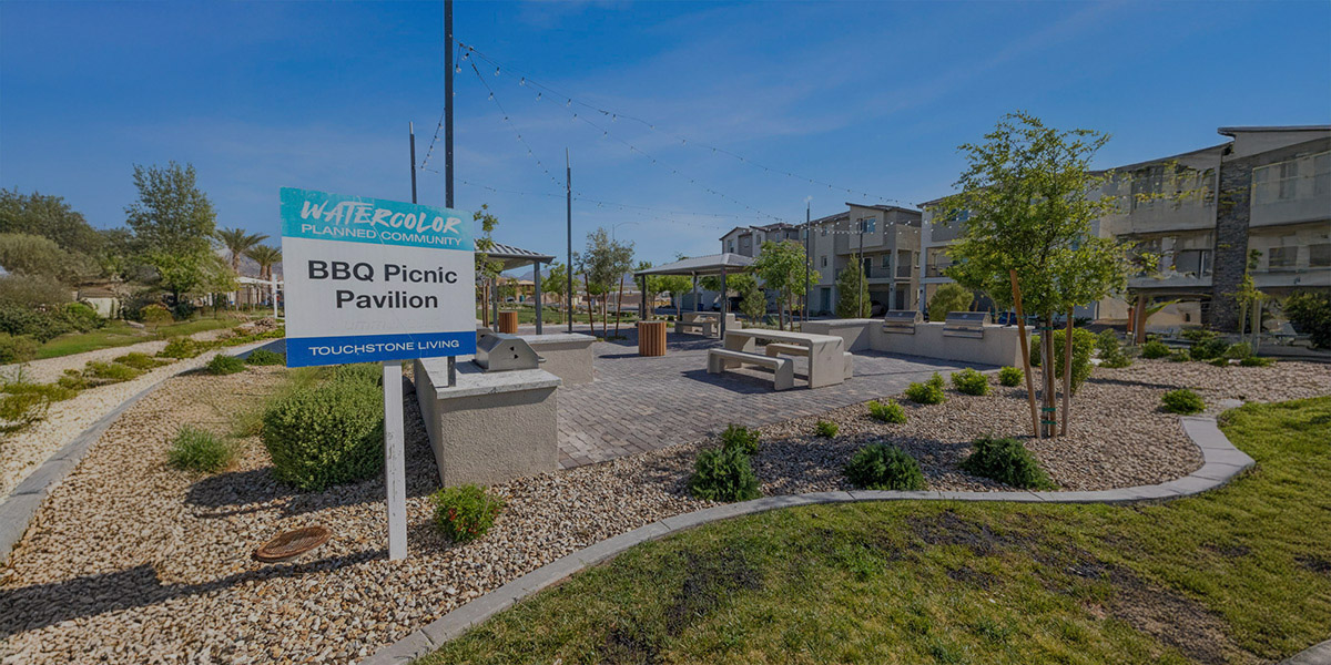 An outdoor community BBQ pavilion with grill and picnic tables and benches