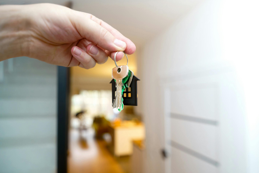an open front white door with a hand holding a set of keys along with a house key chain